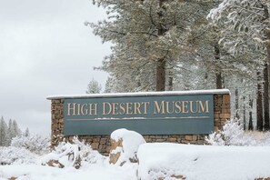 Une enseigne pour le musée High Desert, avec une structure en pierre et en métal, entourée d’arbres couverts de neige.