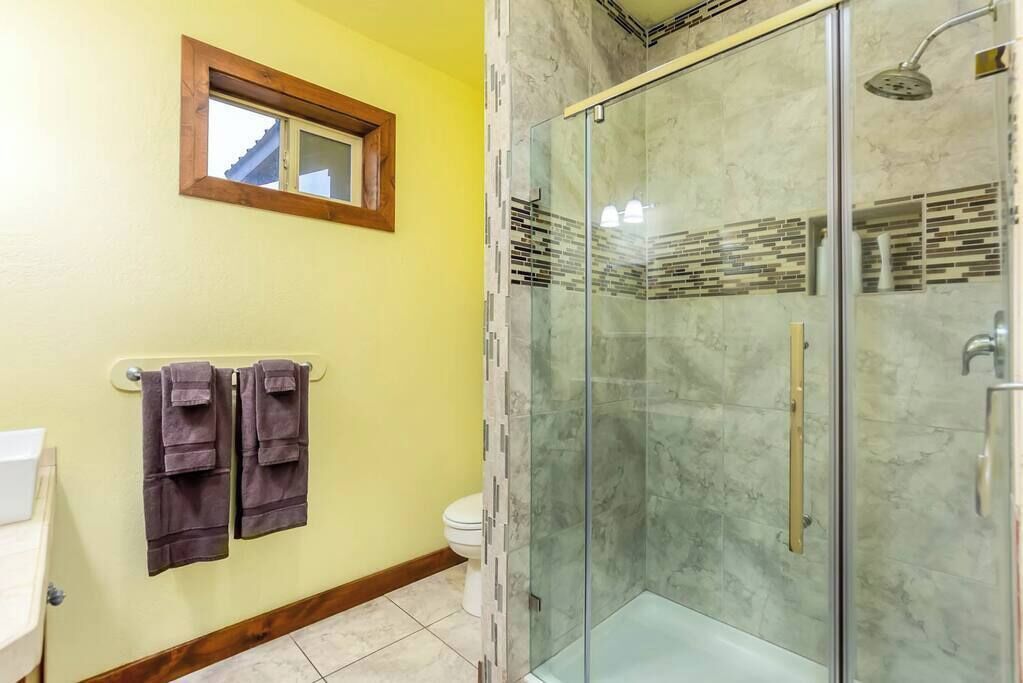 A bathroom with a glass shower enclosure, a toilet, and a towel rack with towels.