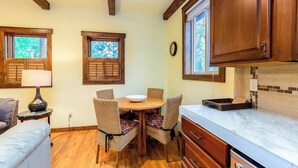 A kitchen with wooden cabinets, a round dining table with chairs, a clock on the wall, and a window with shutters. - Cozy Pet-Friendly Cottage Near Downtown Bend (Bend)