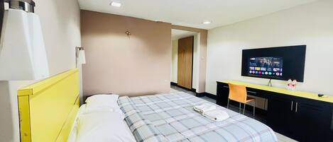 A hotel room with a bed, a desk, a chair, a television, and a door.