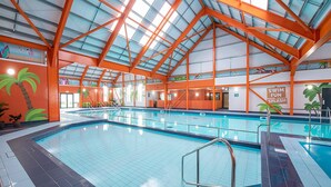 Une piscine intérieure dotée d’un plafond haut et de poutres structurelles orange.