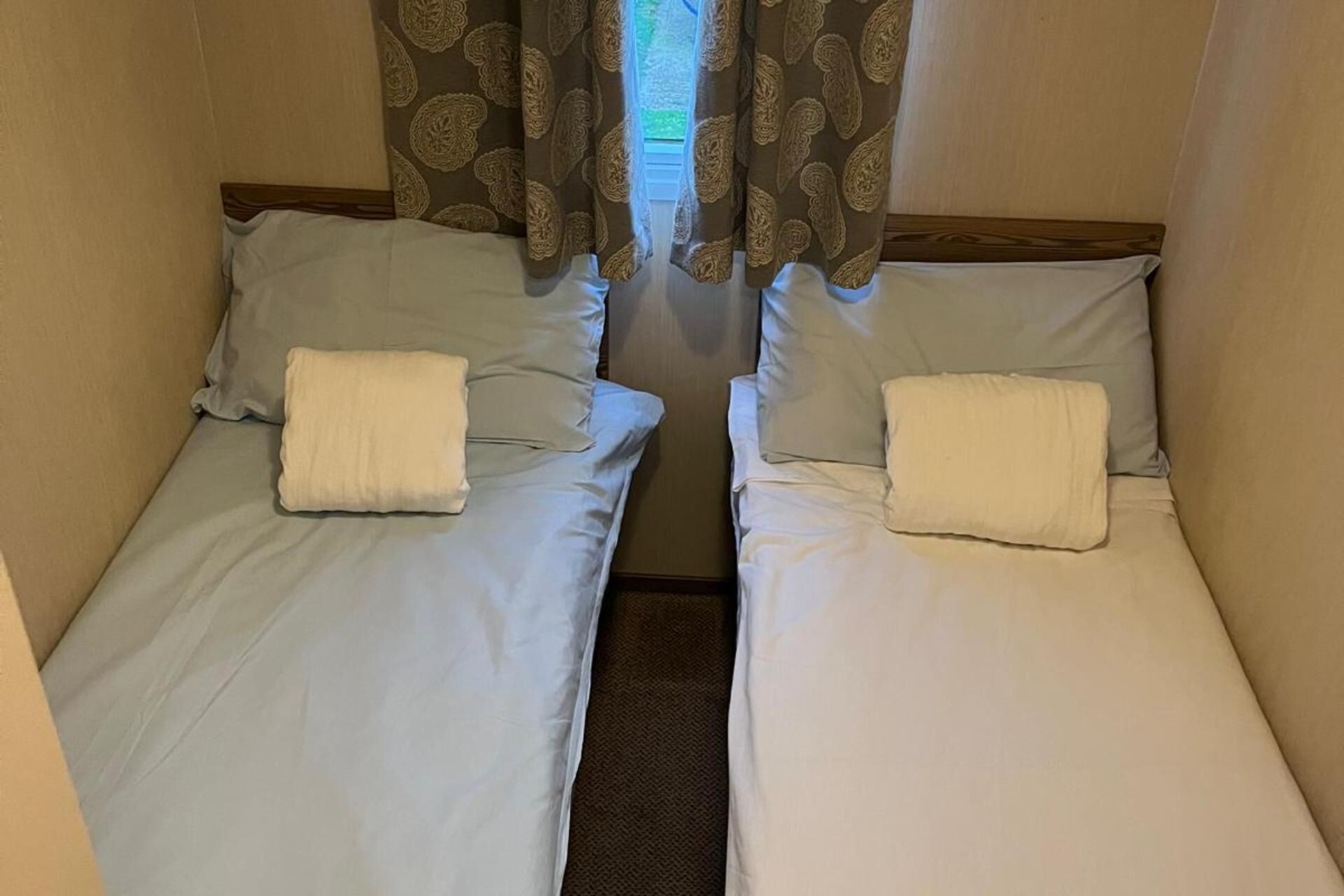 Two single beds with white linens and pillows, a wooden headboard, and patterned curtains.