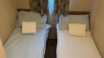 Two single beds with white linens and pillows, a wooden headboard, and patterned curtains.