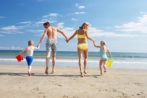 Une famille se promène sur une plage de sable, avec l’océan en arrière-plan.