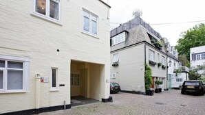 Une ruelle étroite pavée, avec des bâtiments de chaque côté. On y voit des voitures garées et une porte d’entrée bien visible menant à un bâtiment.