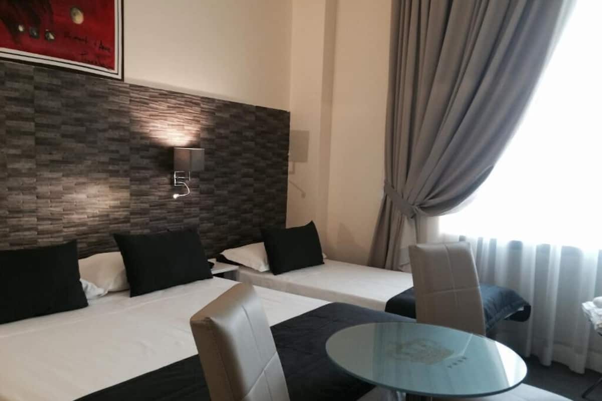 Habitación de hotel con dos camas, una mesita de vidrio y un diseño moderno en la pared.
