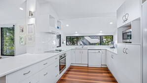 A modern kitchen with white cabinetry, a wooden floor, and a large window providing a view of the outdoors.