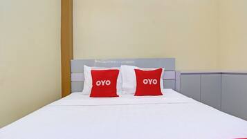 Een hotelkamer met een bed, twee rode kussens met de tekst 'OYO' erop, een witte sprei en een grijze hoofdbord.