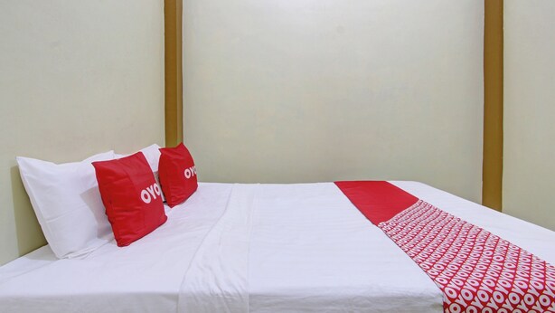 Un lit bien fait, avec une literie blanche et rouge, deux oreillers et une couverture rouge et blanche à motifs.