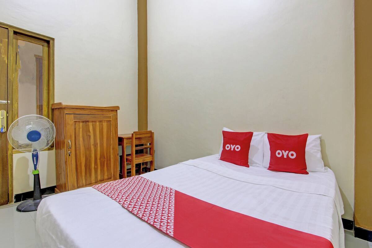 Ein Hotelzimmer mit Bett, Holzschrank, Schreibtisch und Standventilator.