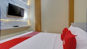 Habitación de hotel con un televisor de pantalla plana grande montado en una pared de mármol, una cama bien hecha con ropa de cama blanca y roja, y un cabecero de madera.