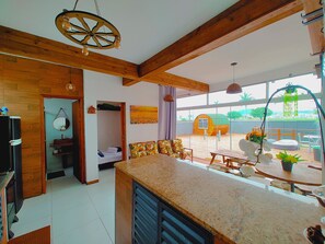 Enjoy a spacious interior with a high ceiling, open-plan kitchen, and dining area, plus a large window offering a view of the outdoor area.