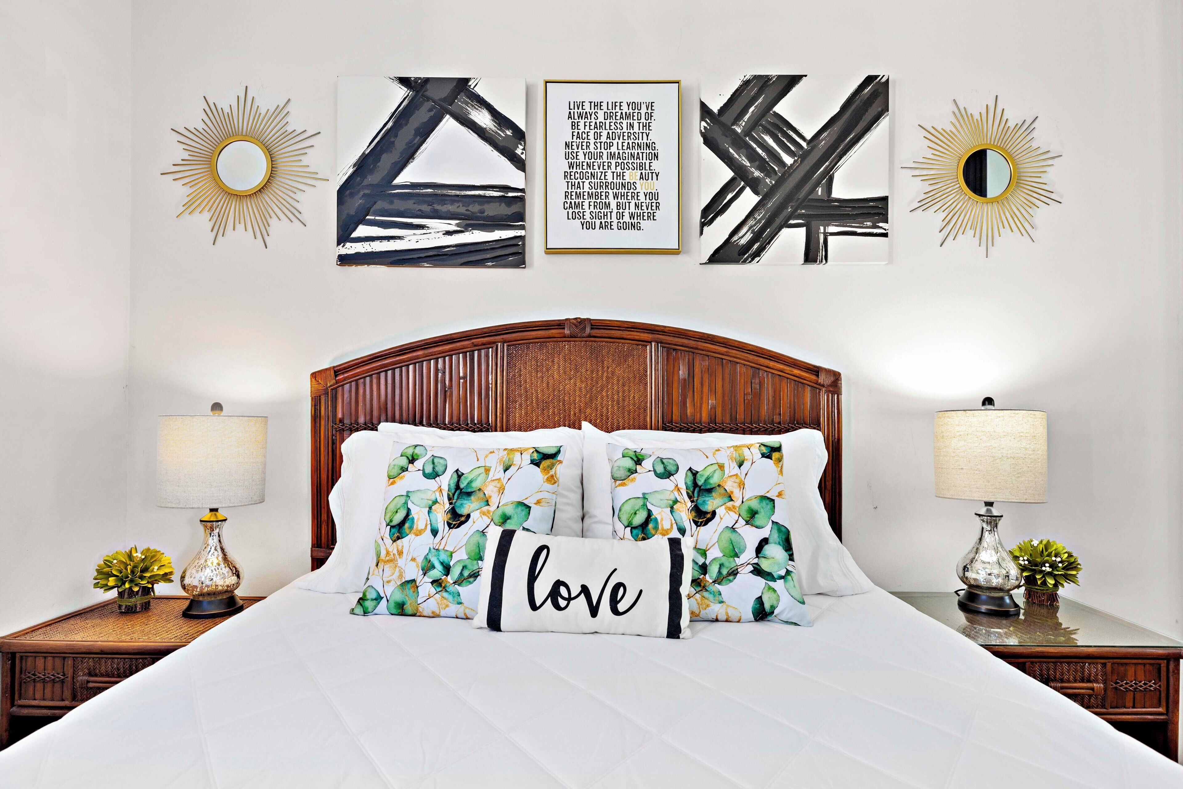 A neatly made bed with floral pillows and a 'love' pillow, flanked by two bedside tables with lamps and decorative vases.