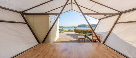 A tent with a wooden floor and a view of a lake.