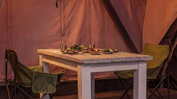 A dining table set up in a tent with various dishes and a metal pot.