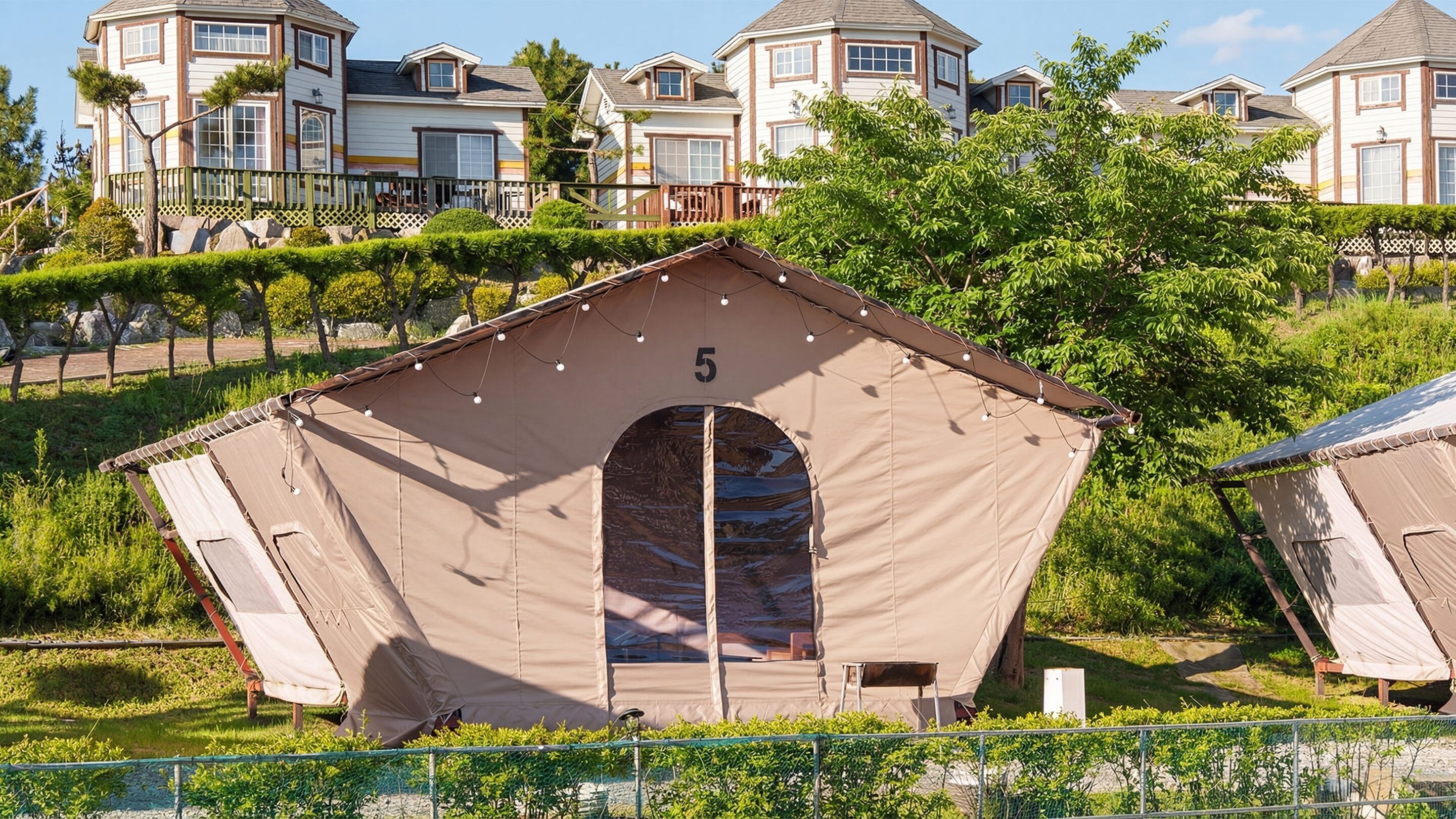 A single-story tent with a number '5' on its front, surrounded by greenery and a fence.