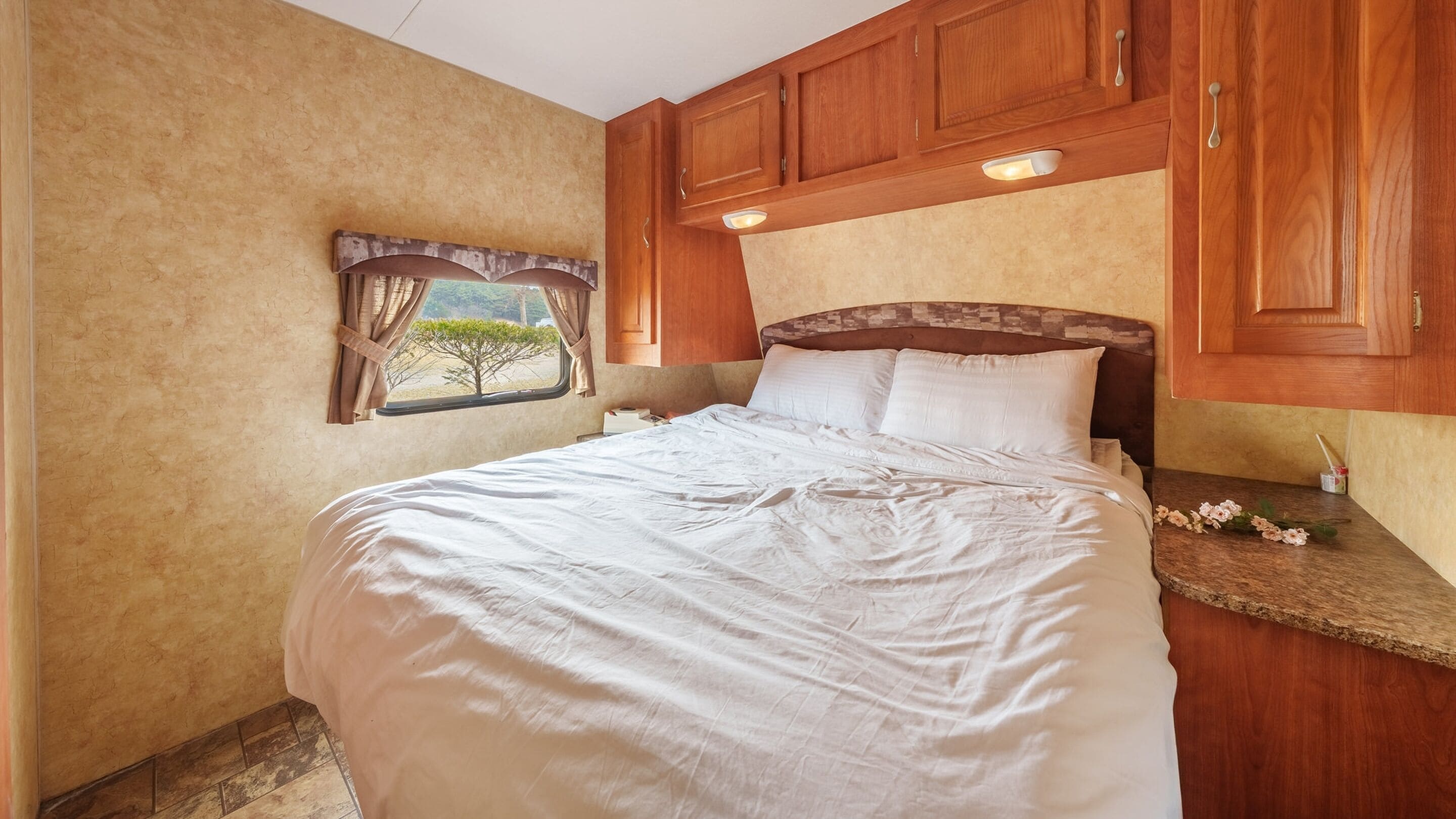 A bedroom with a large bed, wooden cabinets, a nightstand, and a window with curtains.