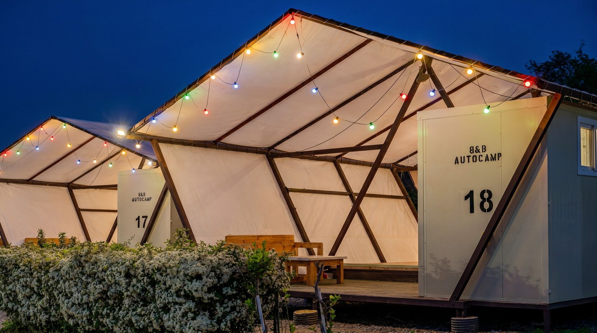 Een tentconstructie met de aanduiding 'B&B AUTOCAMP 18', met het nummer '17' op een andere tent, omringd door begroeiing.