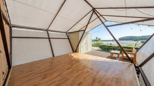 A tented accommodation with a wooden floor, a table, and chairs, and a view of a lake and hills. - Taean Bibi Artglamping (Taean)
