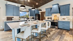 Una cocina moderna con armarios azules, una isla grande, sillas blancas y techo de madera.
