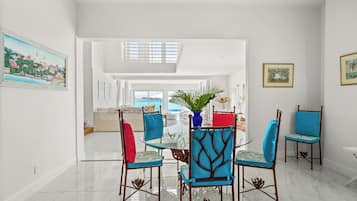 A dining area with a glass table and chairs, a vase with plants, and artwork on the walls.