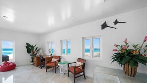 A spacious room with a large window offering a view of the beach, a wooden desk, two chairs, a red bean bag, and a potted plant. - Modern, Stunning & Bright Central Beach Villa (Nassau)