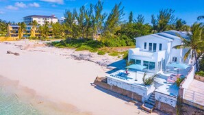 A beachfront property with a modern white building, a swimming pool, and a beach view. - Modern, Stunning & Bright Central Beach Villa (Nassau)