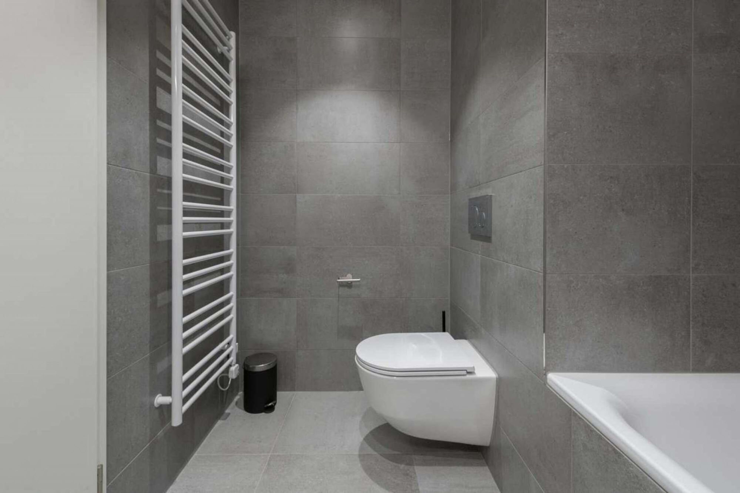 A modern bathroom with a toilet, a bathtub, and a towel rack.