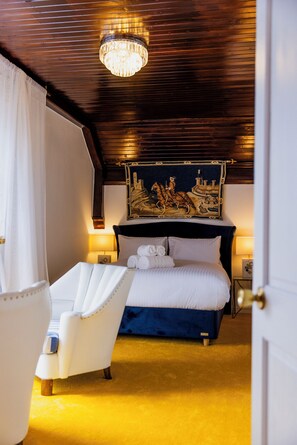 Une chambre à coucher avec un grand lit, un fauteuil blanc, un lustre et un tableau au mur.
