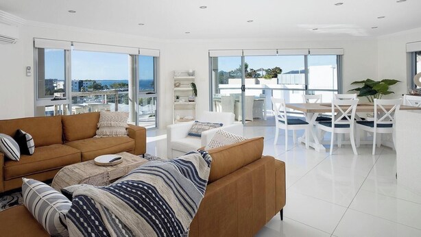 A modern living room with a sofa, a coffee table, and a dining area with chairs and a table.