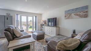 A spacious living room with a leather sofa, a coffee table, and a television. There is a sliding glass door leading to a patio area.