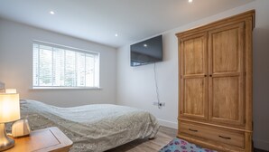 A bedroom with a bed, a wooden wardrobe, a TV mounted on the wall, and a window with blinds.