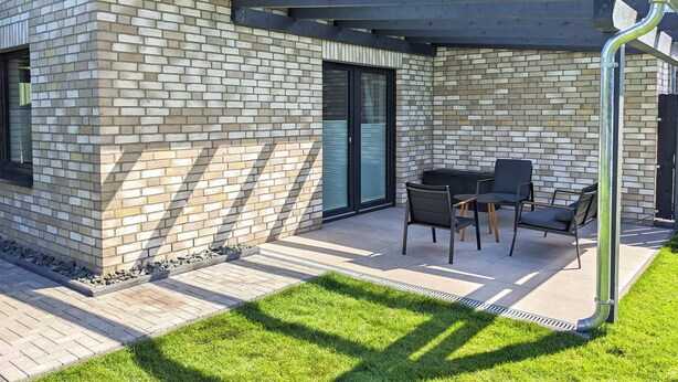 A modern house with a brick exterior, a covered patio with outdoor furniture, and a well-maintained lawn.