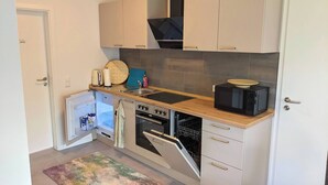A compact kitchen with white cabinets, a built-in oven, a microwave, and a small refrigerator.