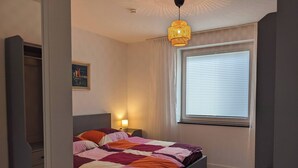 A bedroom with a bed, a nightstand, a lamp, a window with blinds, and a painting on the wall.