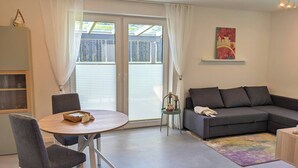 A modern living room with a grey sofa, a round dining table with two chairs, and a small side table with candles.