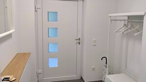 A white door with four square cutouts, a wooden bench, a white coat rack, and a white wall with a mirror.