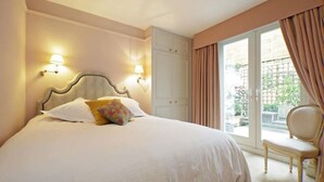 Ein Schlafzimmer mit einem großen Bett, zwei Nachttischlampen, einem Sessel und Blick ins Freie durch eine Schiebetür.