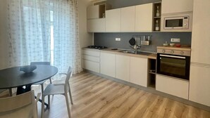 A modern kitchen with white cabinets, a microwave, an oven, and a dining area with a table and chairs. - Walking distance from Vomero, metro within walking distance in area full of clubs.  (Napoli)