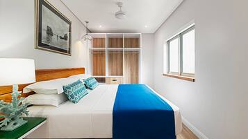 A modern hotel room with a large bed, a wooden headboard, a built-in wardrobe, a bedside table with a lamp, and a framed picture on the wall.