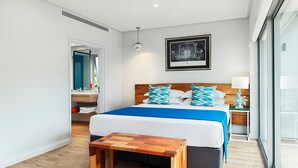 Habitació d'hotel moderna amb un llit gran, una panxa de fusta, una tauleta de nit i una finestra ampla.