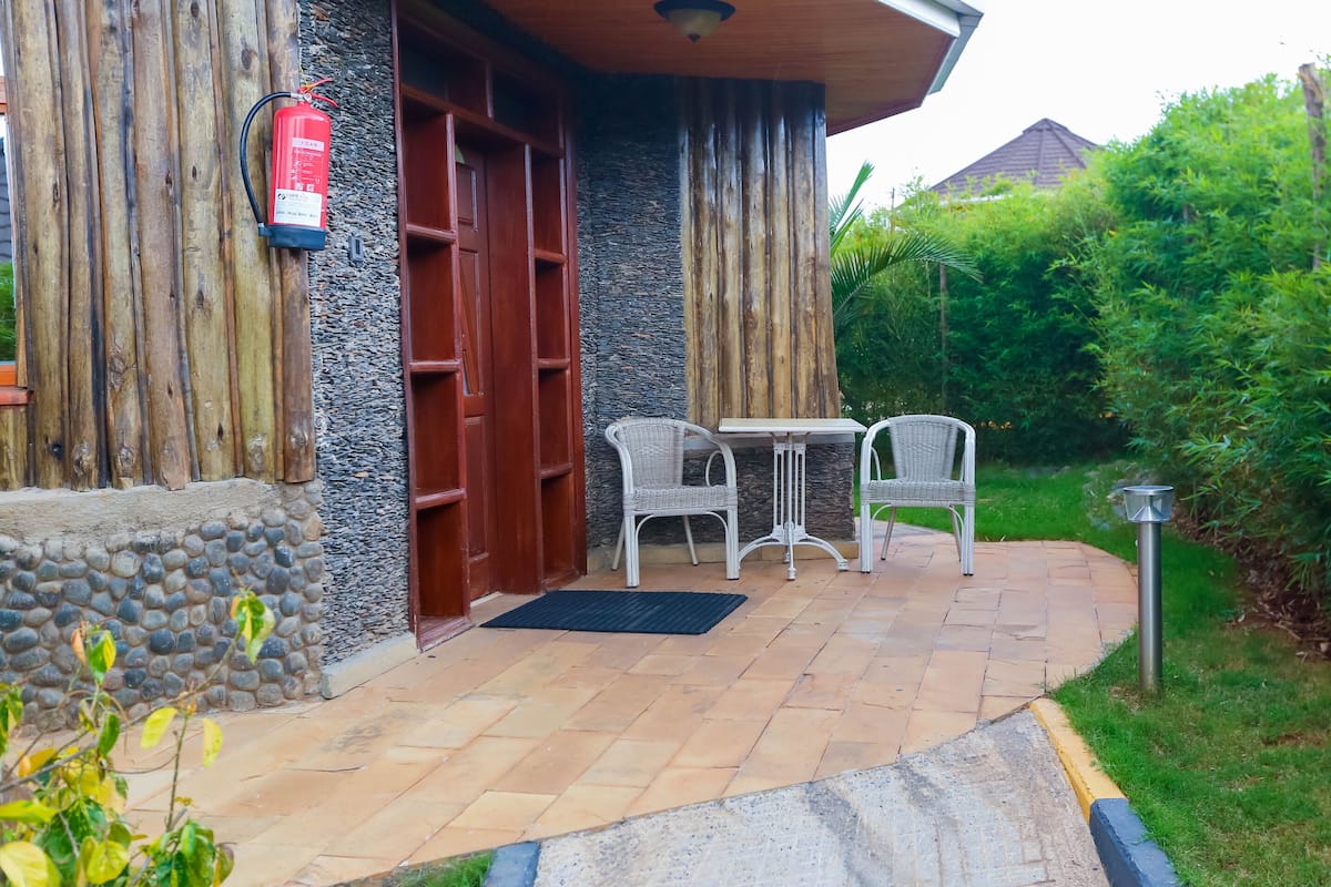 Un edificio con fachada de piedra, una puerta de madera y un pequeño patio con dos sillas de mimbre y una mesa.