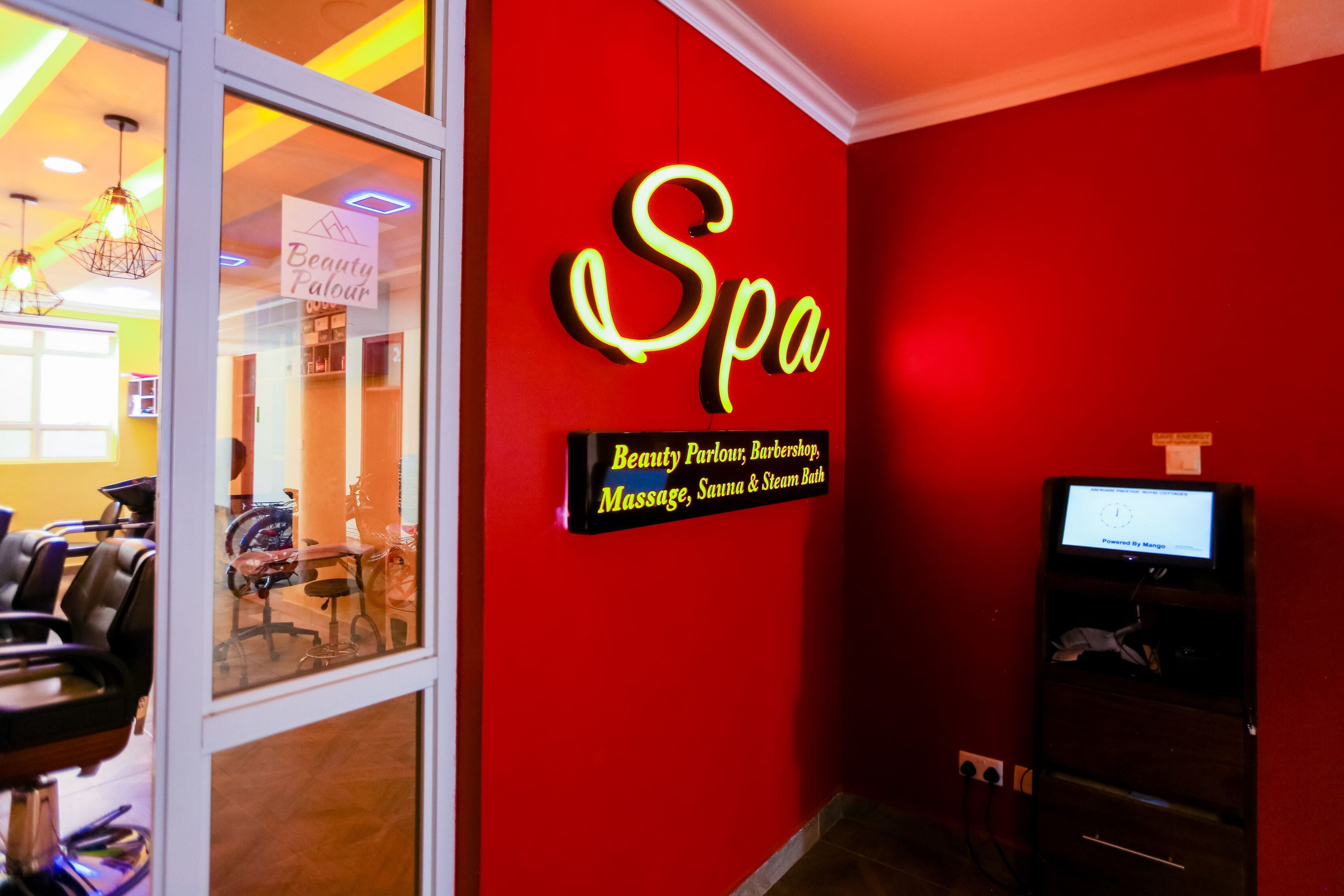 Un mur rouge orné d’un panneau néon indiquant le mot « Spa » et, en dessous, une affiche énumérant les services proposés : salon de beauté, barbier, massages, sauna et bain de vapeur.