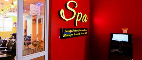 A red wall with a neon sign reading "Spa" and a sign below listing services like beauty parlour, barbershop, massage, sauna, and steam bath.