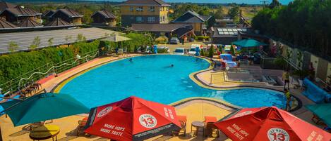 A swimming pool area with lounge chairs and umbrellas, surrounded by buildings and a view of the countryside.