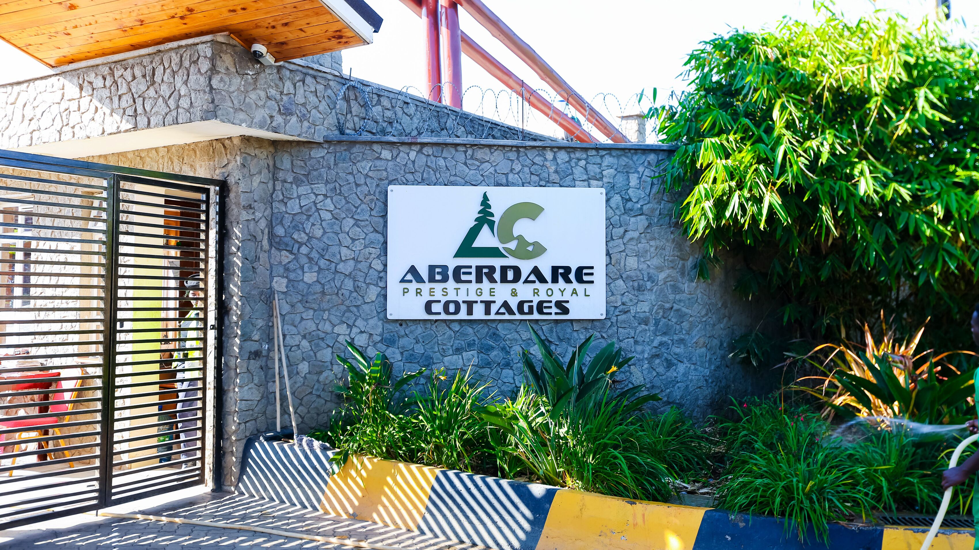 A sign for 'Aberdare Prestige & Royal Cottages' with a stone wall, metal gate, and greenery.