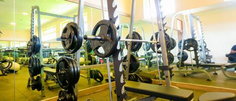 Un gimnasio con equipo de levantamiento de pesas, una banca y un espejo que refleja la sala.