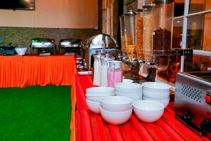 A buffet setup with various food dispensers and white plates arranged on a red table.