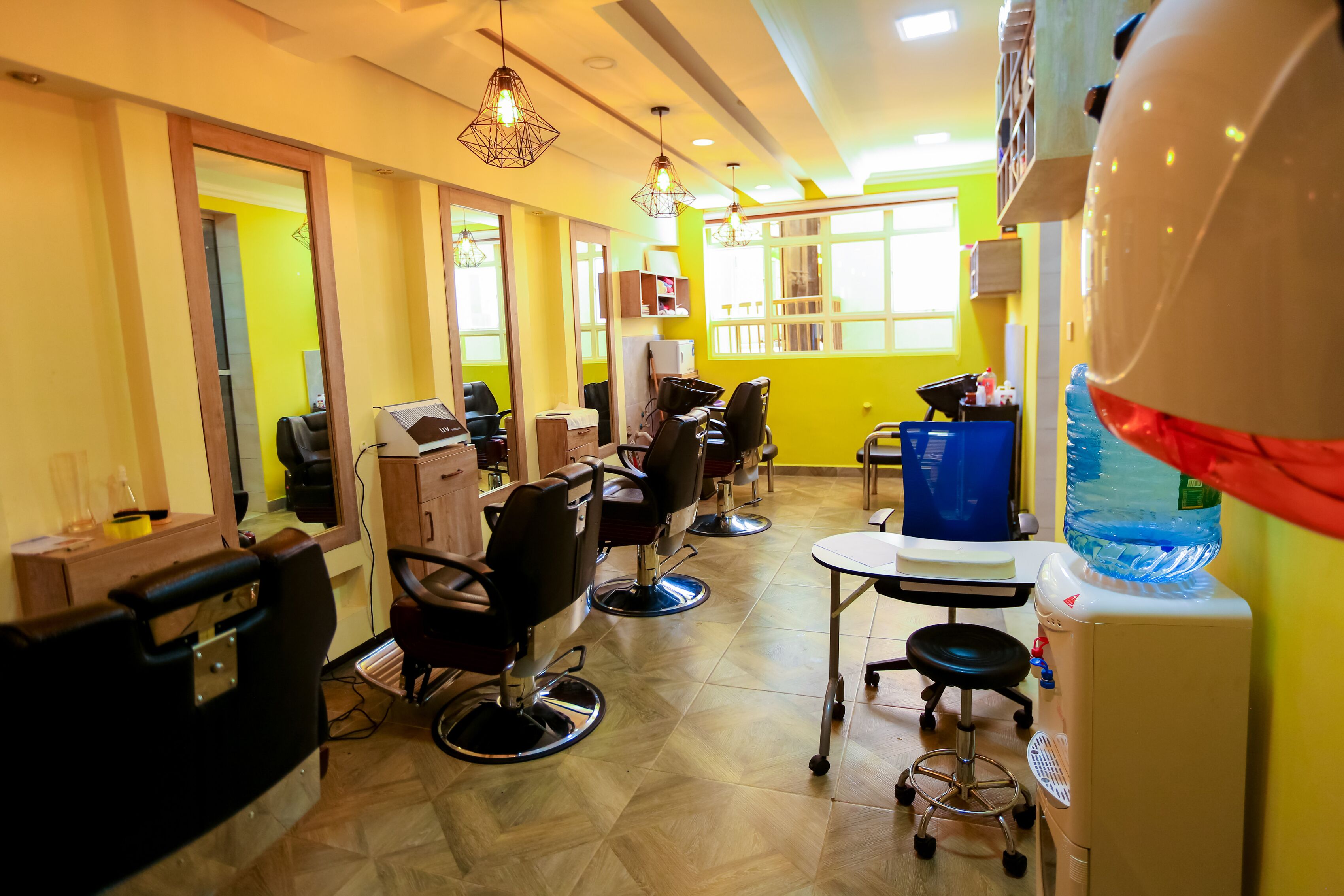 A salon with multiple chairs, a mirror, and a water dispenser.