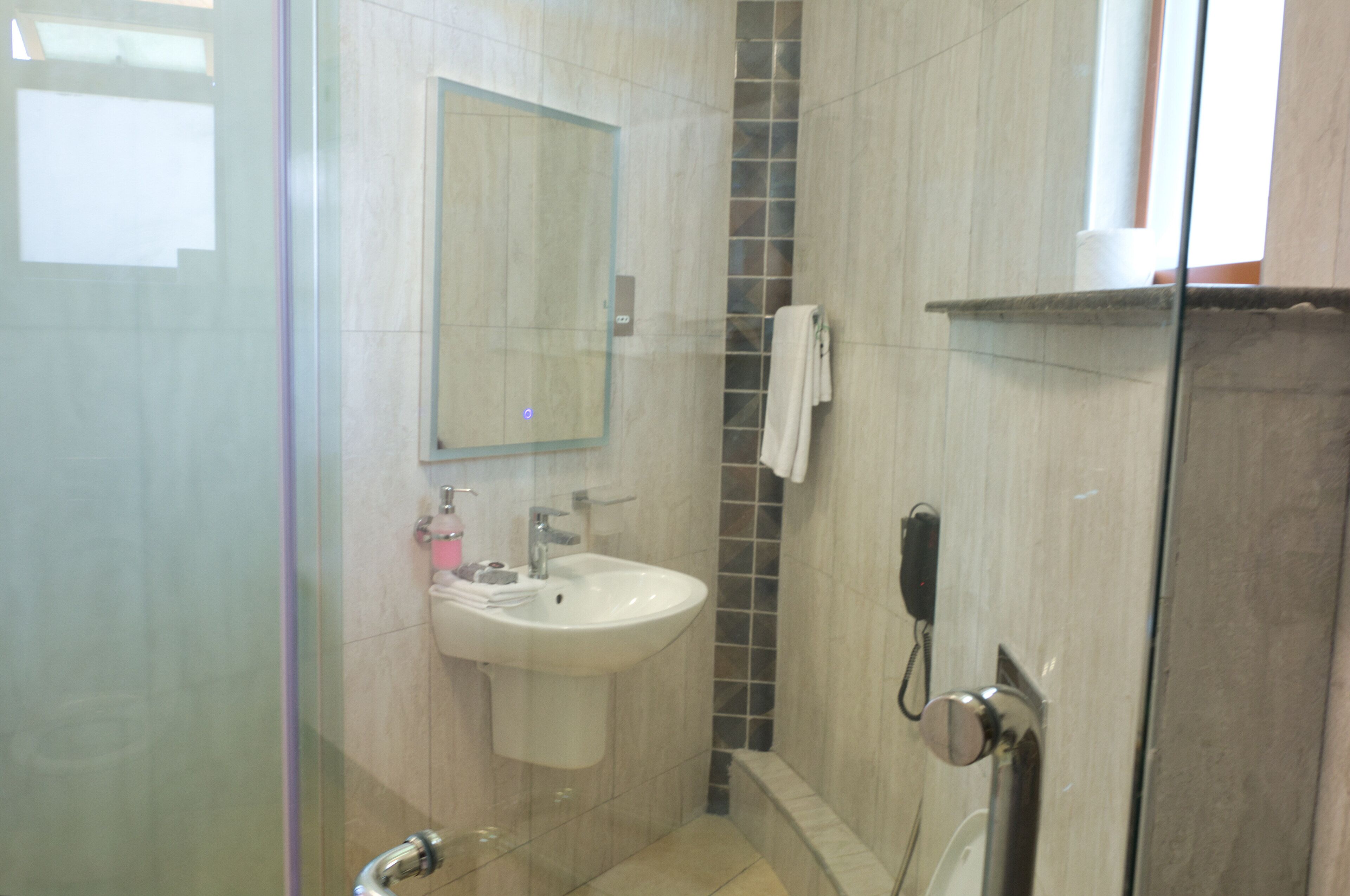 A bathroom with a glass shower enclosure, a sink with a mirror above it, and a towel hanging on the wall.
